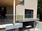 Ringhiera del balcone in vetro con corrimano in acciaio inox e con pannelli in vetro stratificato fissati con borchie
